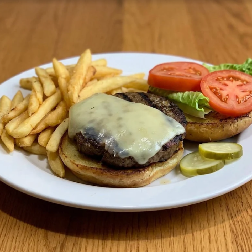 Plate featuring a cheeseburger, a lettuce-and-tomato burger, French fries, and pickle slices on a wooden table.
