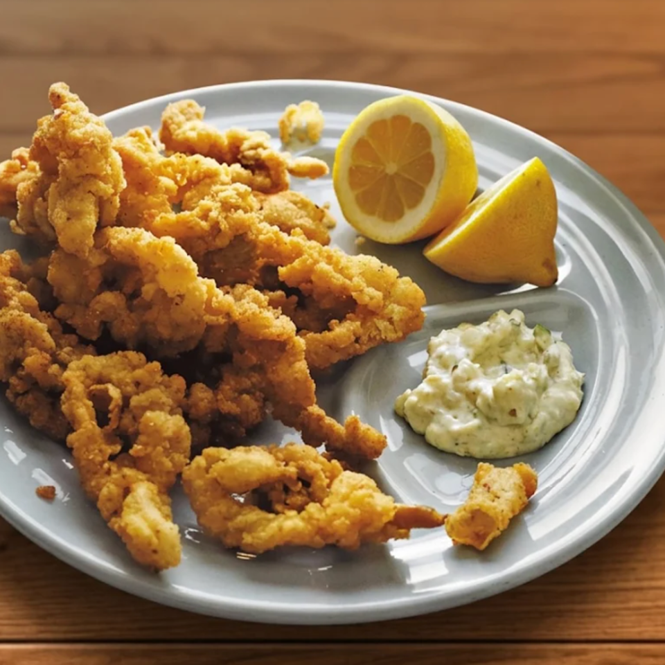 Plate of golden fried calamari with lemon wedges and creamy dipping sauce on a wooden table.